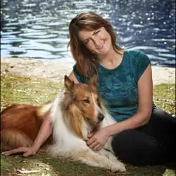 Woman sitting on grass with a rough collie by a lake