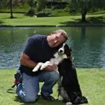 Man kneeling with a dog beside a pond